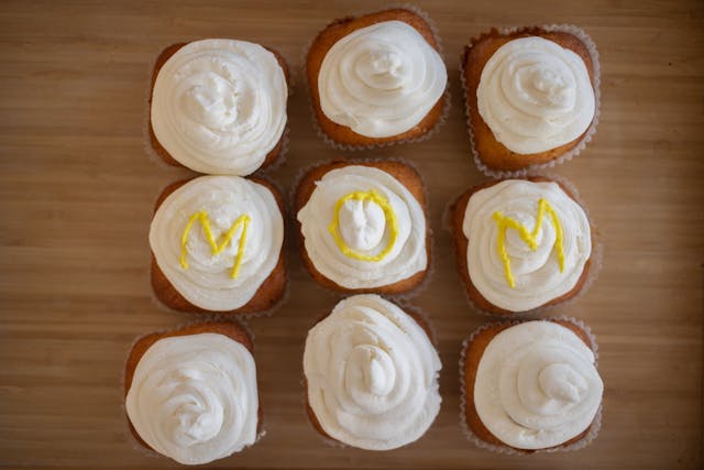 Twelve Bahama Mama cupcakes topped with white icing spelling ‘mom’ in yellow icing