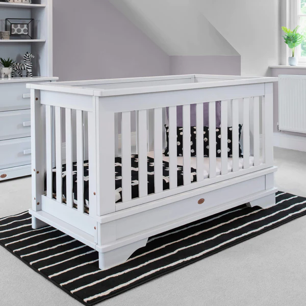 Image: A white wooden cot bed standing on a black striped rug in a white nursery A white wooden cot bed standing on a black striped rug in a white nursery