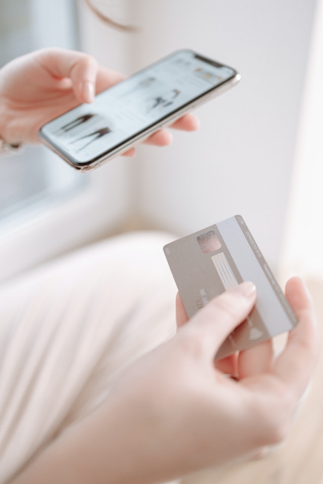 Amex gold card: A person holding a phone and credit card whilst sitting down
