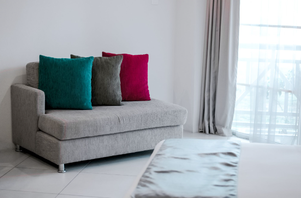 Image: A single sofa bed with 3-different colour cushions placed next to a window A single sofa bed with 3-different colour cushions placed next to a window