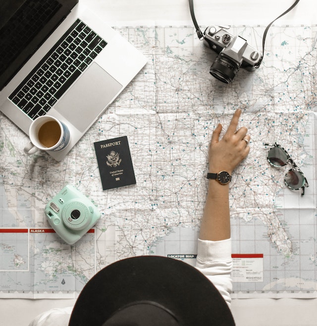 Best travel credit card: person pointing at a map with a camera, passport, laptop and coffee on it