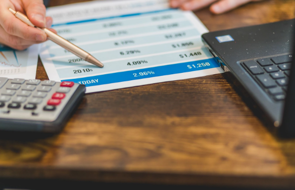 Cash ISA rates nationwide displayed on a paper on a desk next to a calculator, laptop and hand holding a pen.