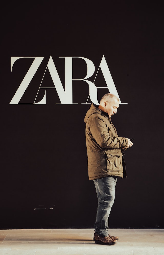 Barbie clothing for women: Man standing busy with his phone under the ZARA shop logo in white and bold.