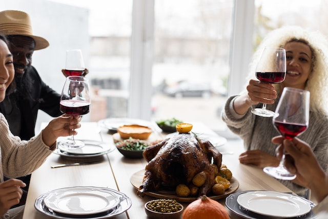 Four friends making a toast around a roast chicken dinner with glasses of wine