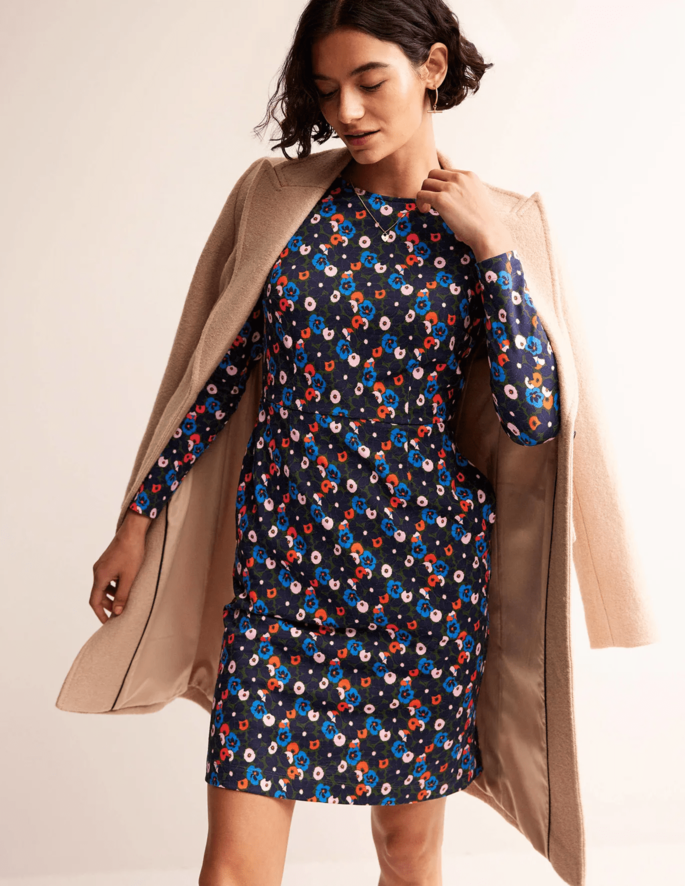 A model posing in a Penelope jersey dress in front of a beige background