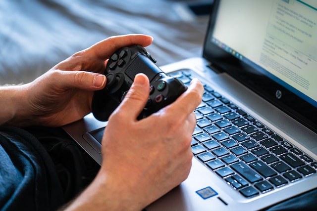 A person holding a black game controller while playing on an HP gaming laptop