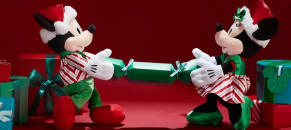 Mickey Mouse & Minnie Mouse soft toys pulling on a Christmas cracker with Disney gifts for Christmas next to them.