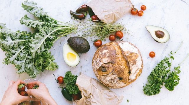 A wonky veg box laid out across a marble countertop around a loaf of bread