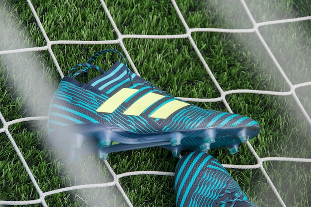 A pair of blue and yellow Adidas football boots in a net on top of the grass