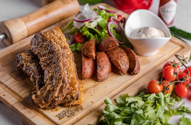 Meat, sauce and vegetables on a brown wooden with tomatoes and herbs next to the chopping board