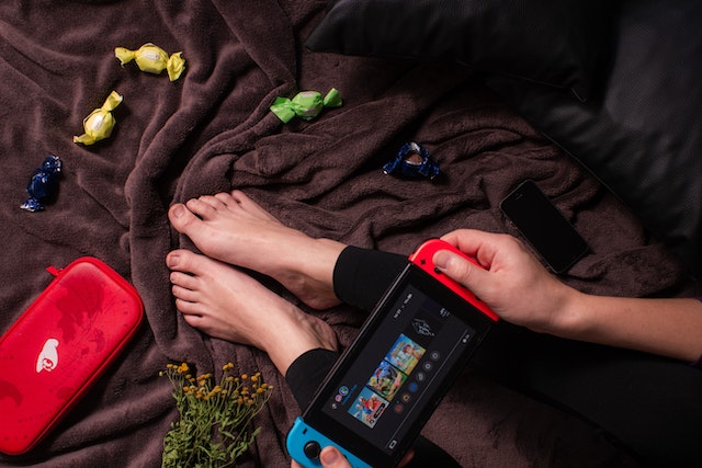 A person playing Nintendo Switch games for cheap on their bed with snacks