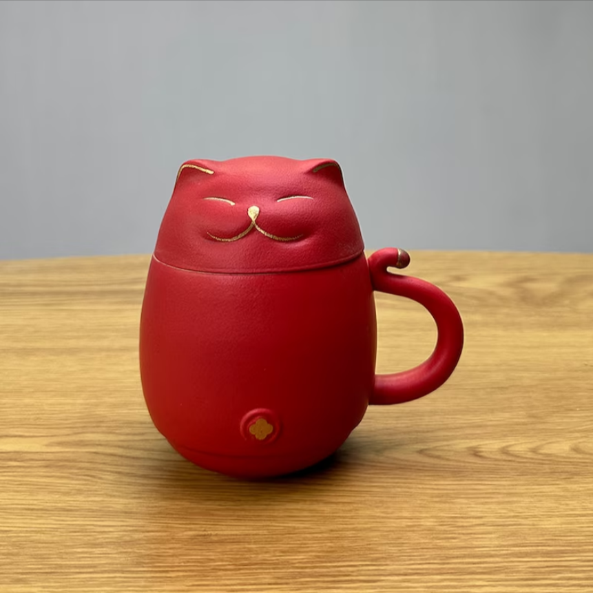 A red cat tea mug and lid with gold details on the face, handle and ears