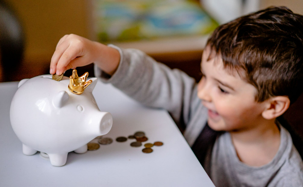 A boy placing money into his piggy bank for his money-saving challenge.
