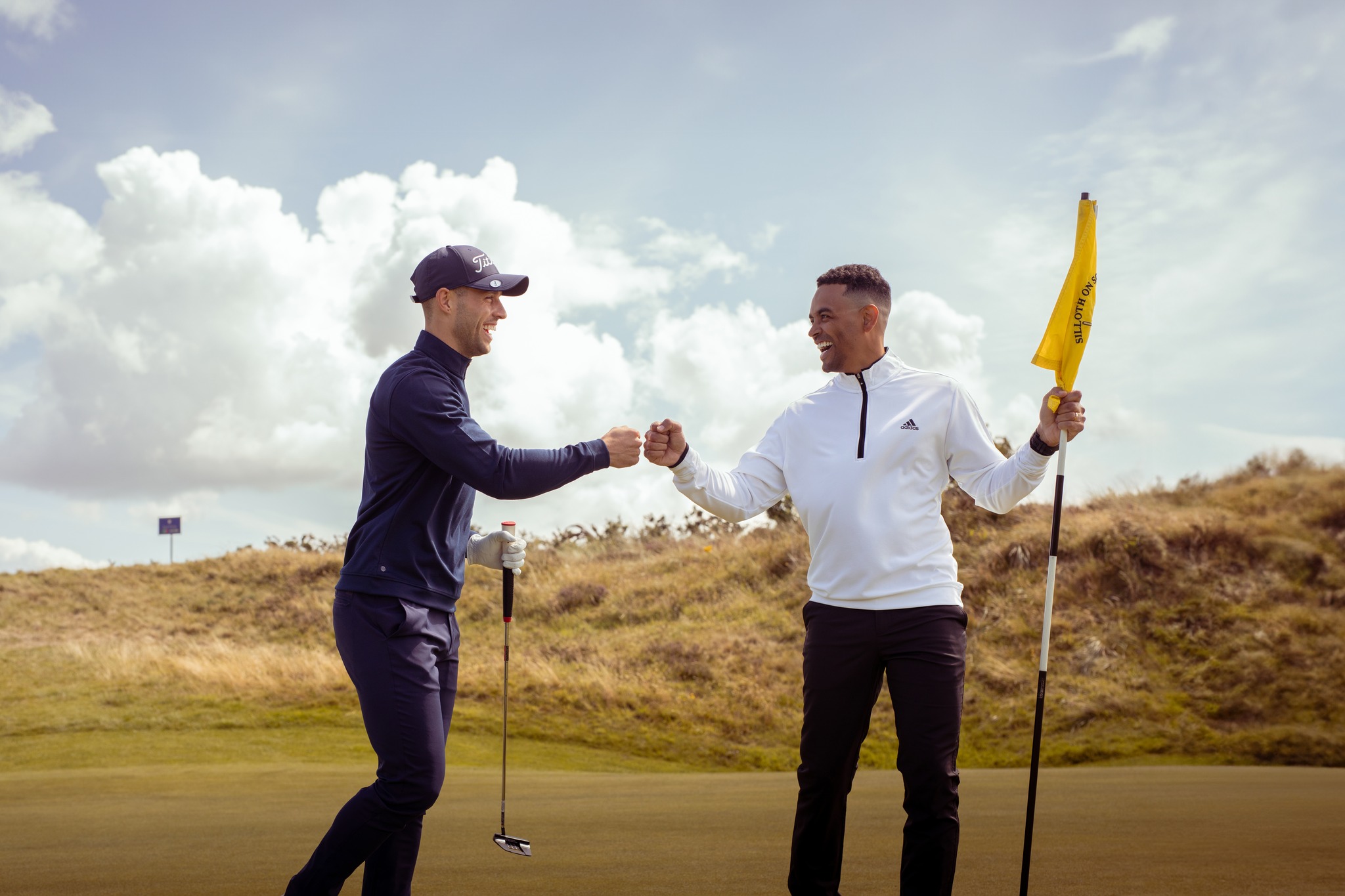Image: Two men in tracksuits fist-bumping on a golf course while holding golf equipment Two men in tracksuits fist-bumping on a golf course while holding golf equipment