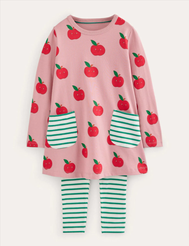 Image: A pink tunic with red apples and green & white striped leggings laying on a beige background A pink tunic with red apples and green & white striped leggings laying on a beige background