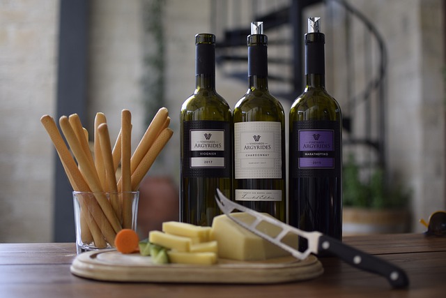 Bottles of wine with a variety of cheeses on a cheese board and a cheese knife all set for cheese and wine tasting.