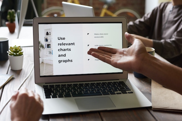 A person pointing at the screen of their cheap HP laptop while sitting at a table