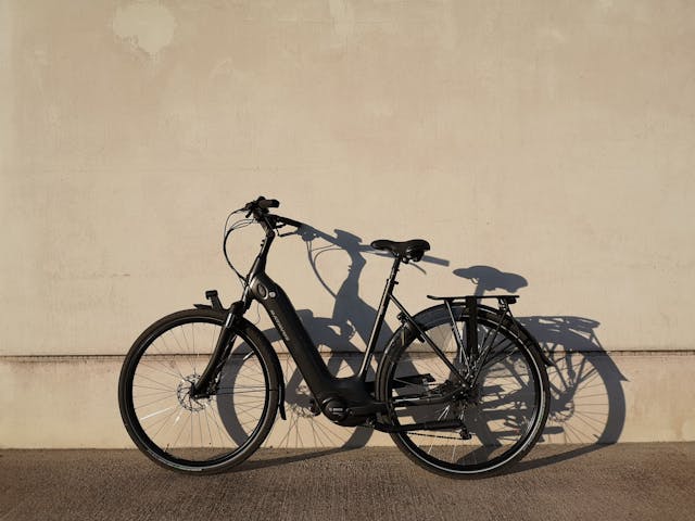 A black electric bike that has been placed against a wall outside