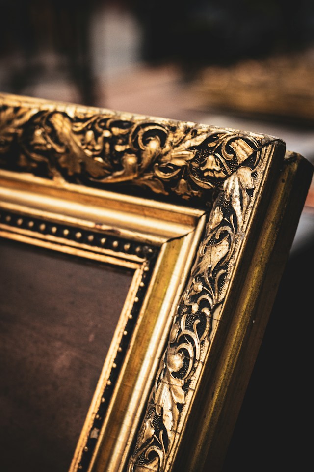 An empty antique gold-painted wooden picture frame leaning against a table