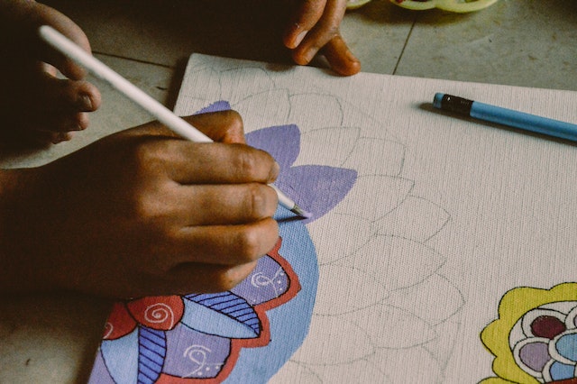Person painting colourful flowers on a white canvas as gifts for Mother’s Day