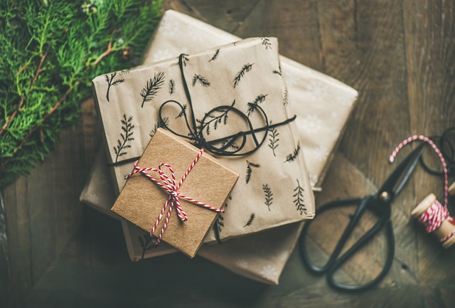 On a wooden table, wrapped presents decorated with bows next to green foliage and a pair of scissors