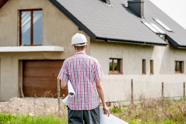 What is the process of buying a house?: Man wearing a hard hat and holding a house plan looking at the house.