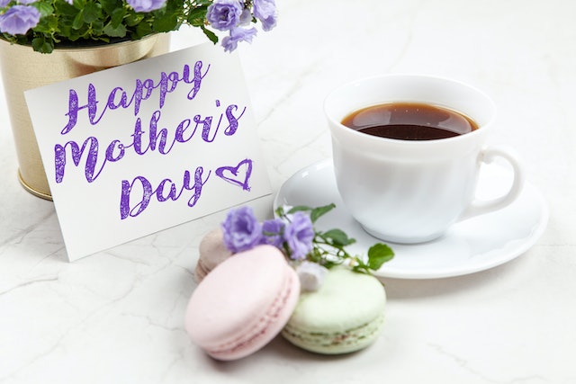 A Mother’s Day card, a flower vase with flowers, a teacup and saucer and macarons for Mother’s Day