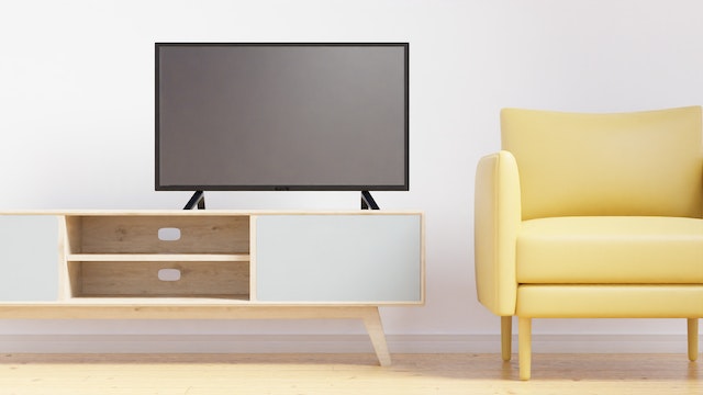 A Samsung 55 inch smart TV standing on a tv stand next to a yellow couch
