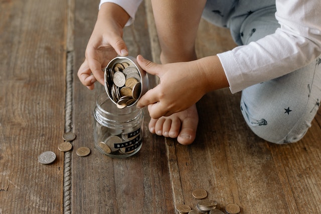 A kid pouring coins in a jar to save them.