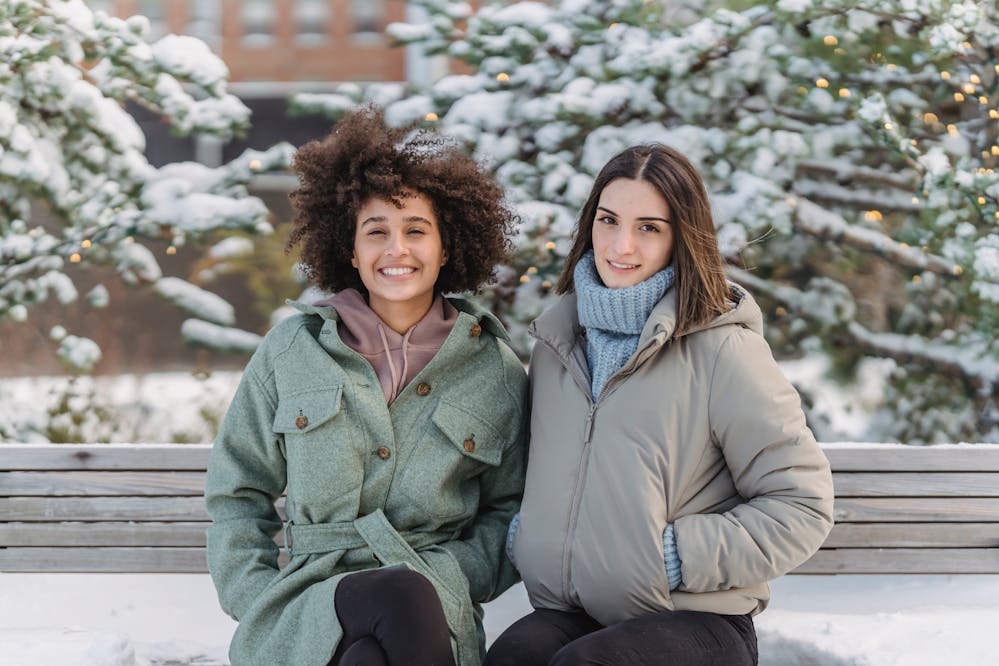Two women on a bench wearing women’s winter coats and jackets