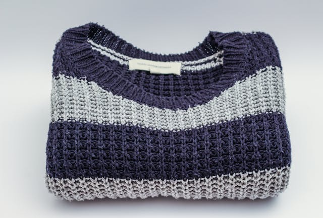 Women's knitwear (NZ): A folded blue and grey sweater on a white surface