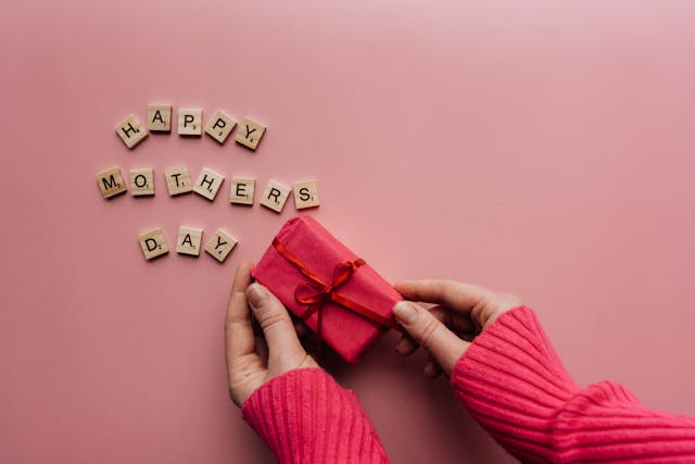 Custom Mother's Day gifts: Mother’s Day scrabble tiles and a pink gift box in a person’s hands