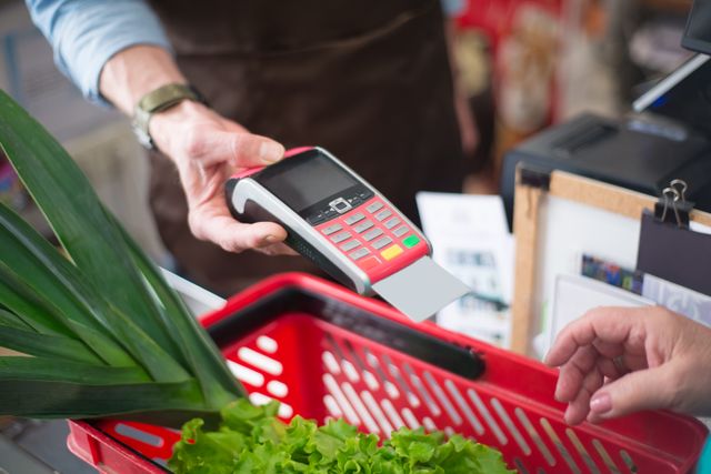 How to save money on food: A person holding out a payment terminal for a grocery purchase