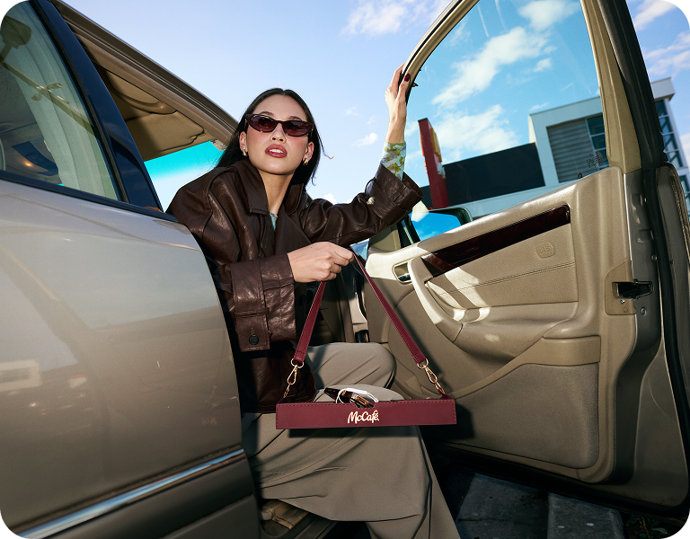 A woman stepping out of a car while holding a McCafe tray bag