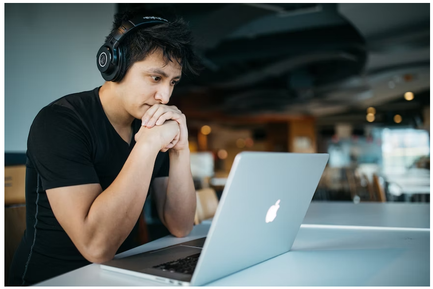A male student wearing his headphones, browsing on his laptop for a Boat promo code