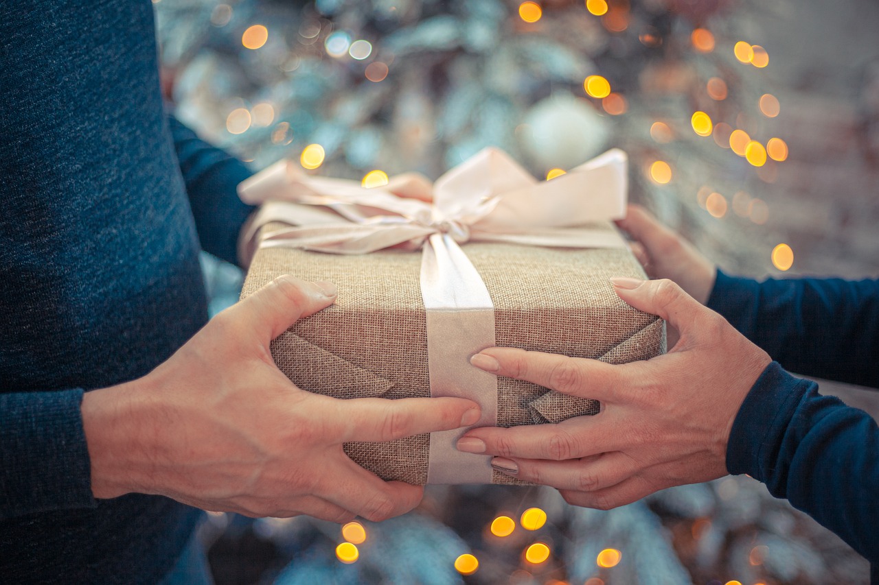 un hombre y mujer se dan un regalo envuelto detrás de un arbol disponible con las ofertas de regalos y ocasiones