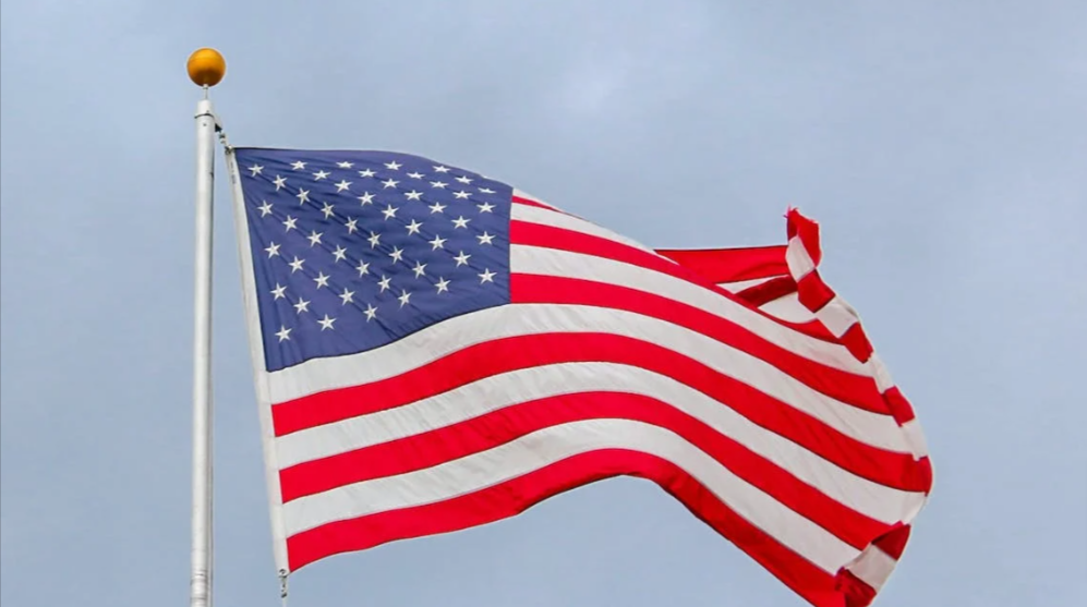 American flag on a flag pole raised into the air. It is being blown by the wind.