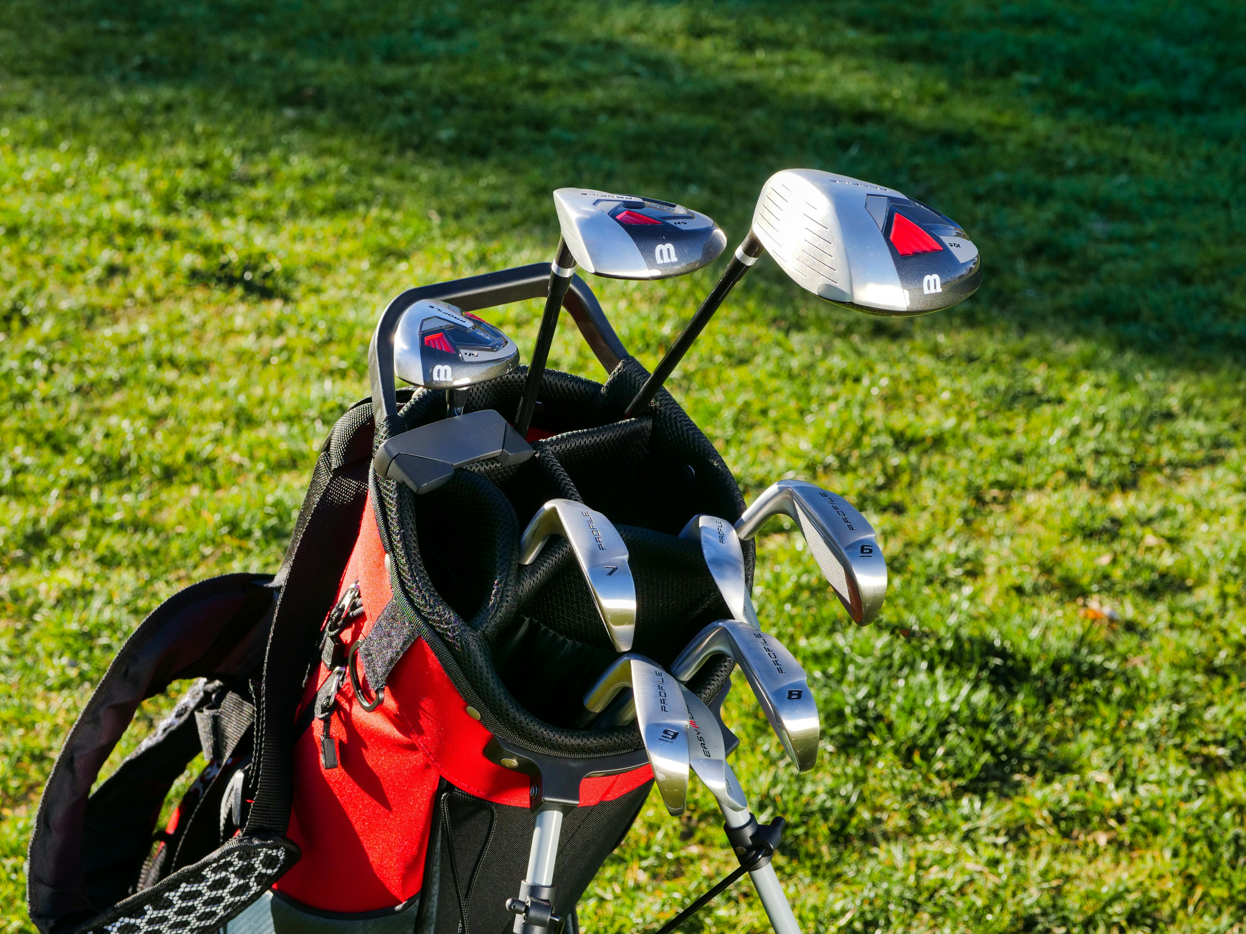 A golf bag with golf clubs in an open space on a green field.