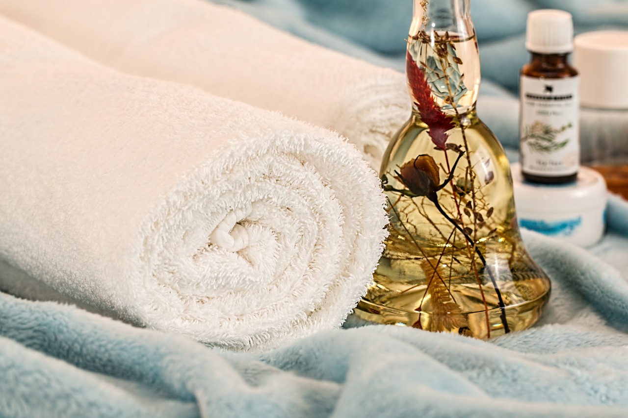 unas toallas sobre un manto azúl junto con cosméicos y un liquído amarillo con plantas