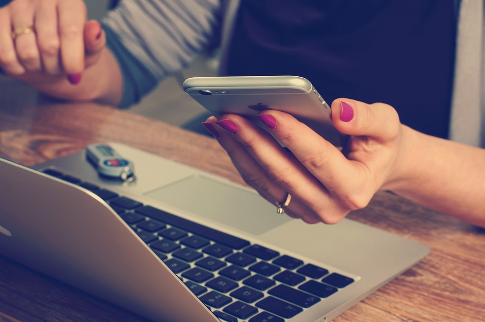 studentessa con un cellulare in mano mentre cerca un codice sconto asgoodasnew sul proprio laptop per risparmiare sui prodotti