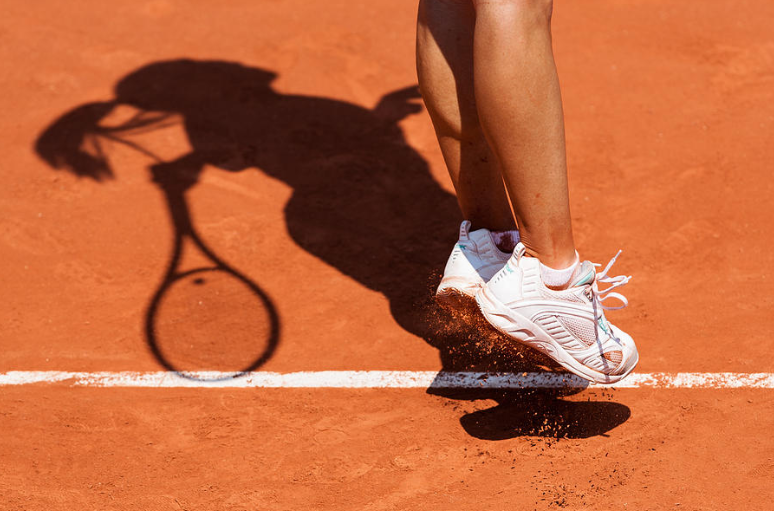 Woman tennis player jumping to hit the tennis ball with her shadow showing on a clay court