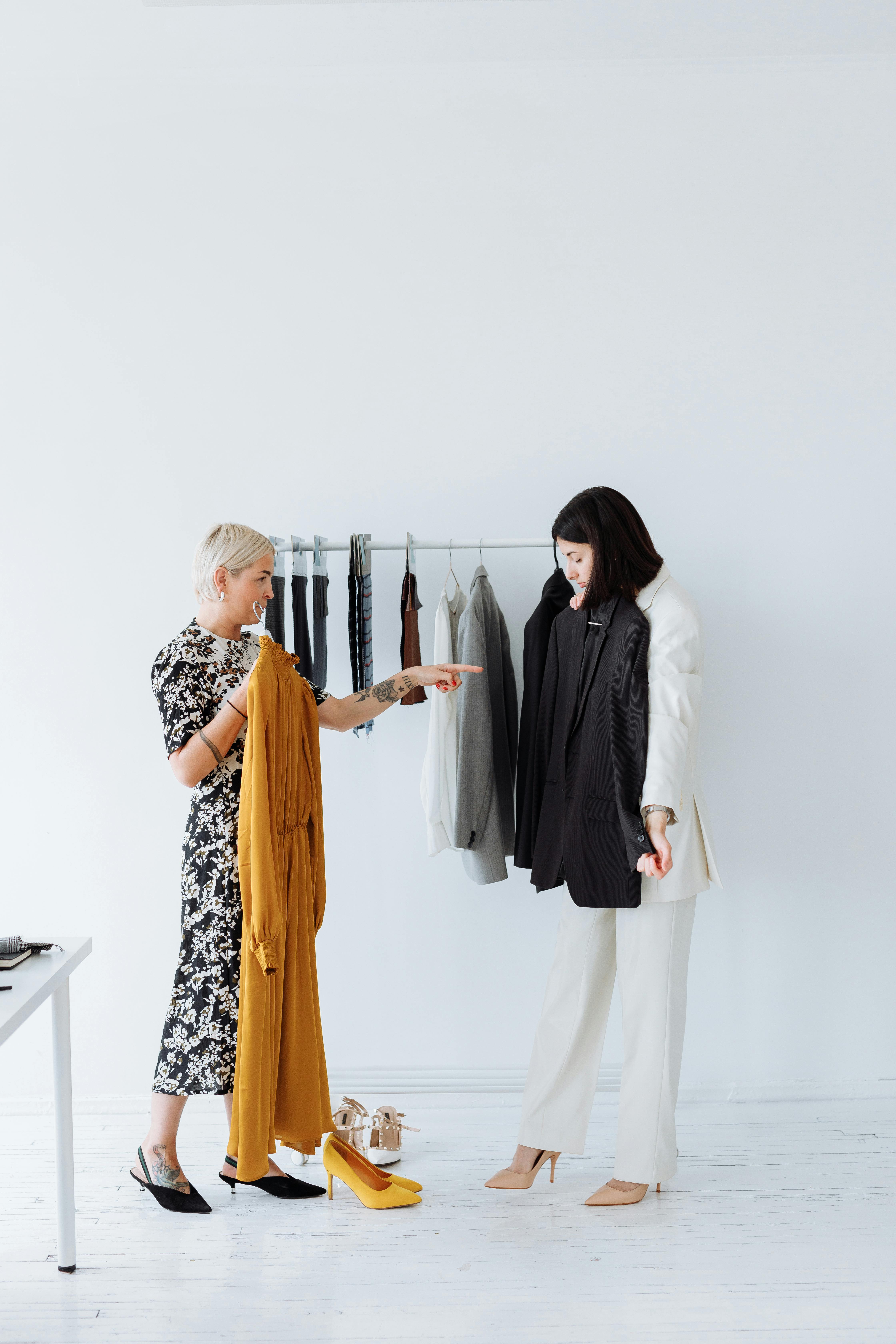 A woman holding a black blazer while standing next to a clothes rack.