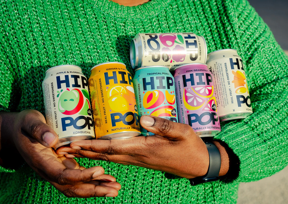 A person in a green jumper holding six cans of HIP POP prebiotic soda
