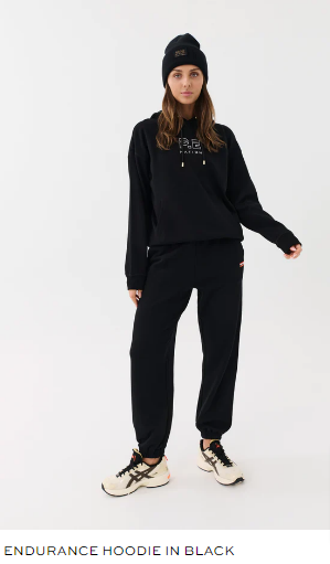 Standing against a white background is a woman in a black endurance hoodie.