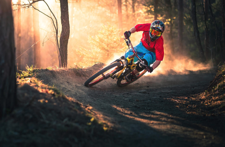 Biker wearing a red top and a helmet turning on his side on a gravel sand road in the woods