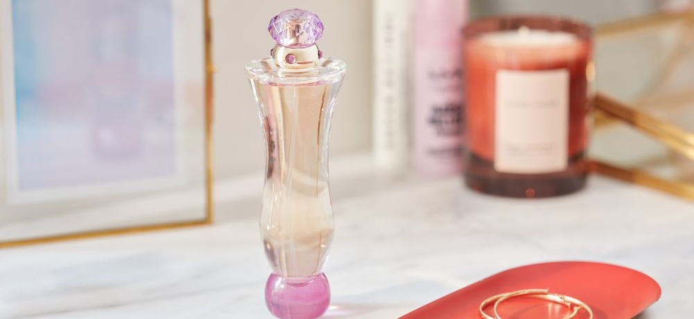 Women's perfume bottle on dressing table with hoop earrings next to it and a scented candle in the background