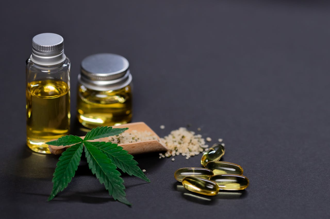 CBD oil and capsules with seed and a hemp leaf with a black background.