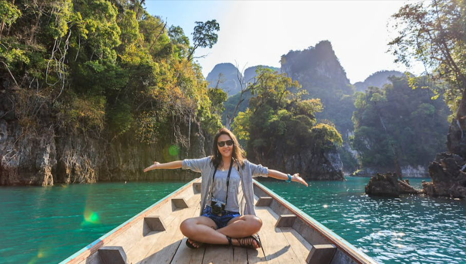 Woman sitting on a canoe spreading her arms and enjoying a canoeing activity with her partner with a mountainous tropical background