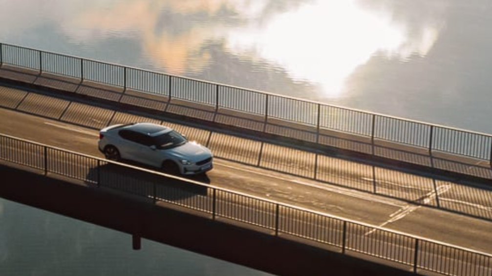 Ein einsames Auto in Weiß, welches auf einer Brücke entlang fährt mit einem See darunter