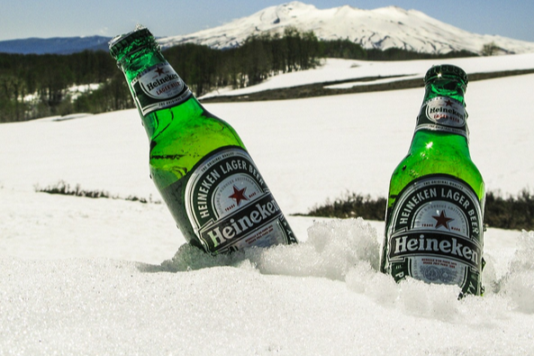 Zwei grüne Bierflaschen im Schnee mit Wäldern und einem Berg im Hintergrund